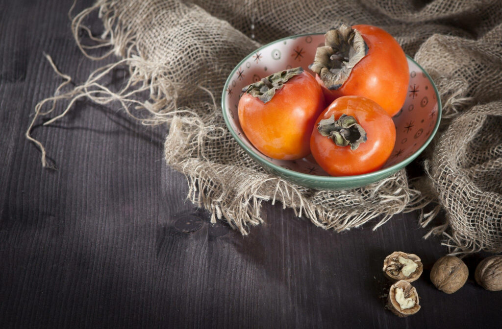 Vibrant Persimmons in Rustic Bowl: Cozy Organic Wallpaper Background