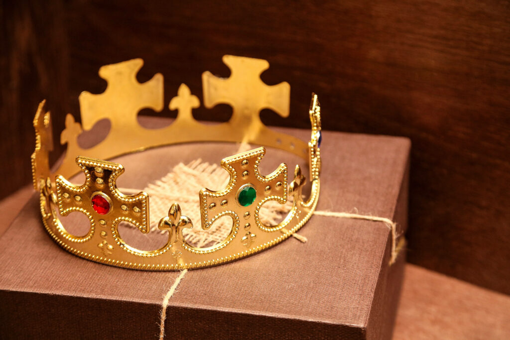 Colorful plastic king and queen crowns with gems on brown gift box rustic wooden background Wallpaper