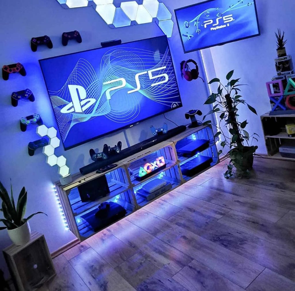 Vibrant PlayStation 5 gaming setup wallpaper with blue LED lights wall-mounted controllers and wood shelf