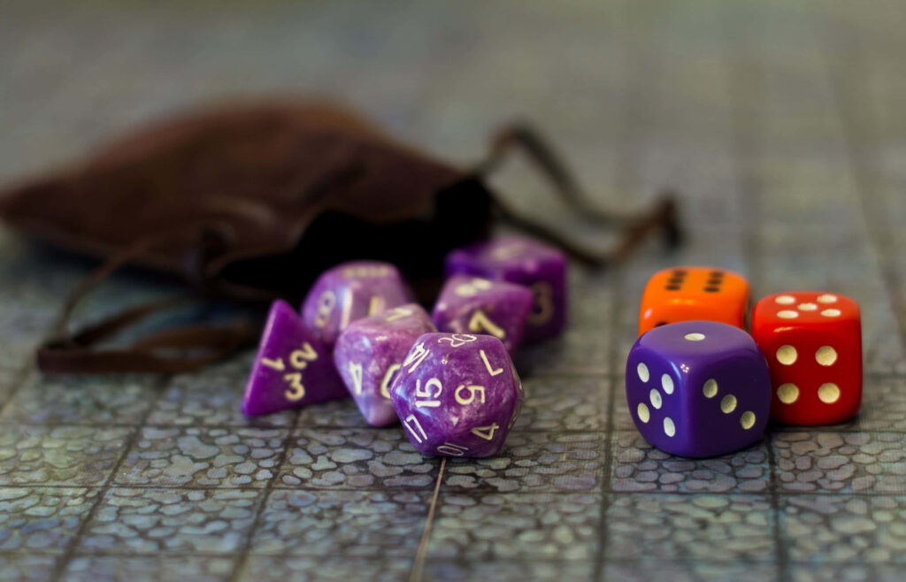 Vibrant purple polyhedral and classic red orange dice scattered on textured game board with brown pouch Wallpaper