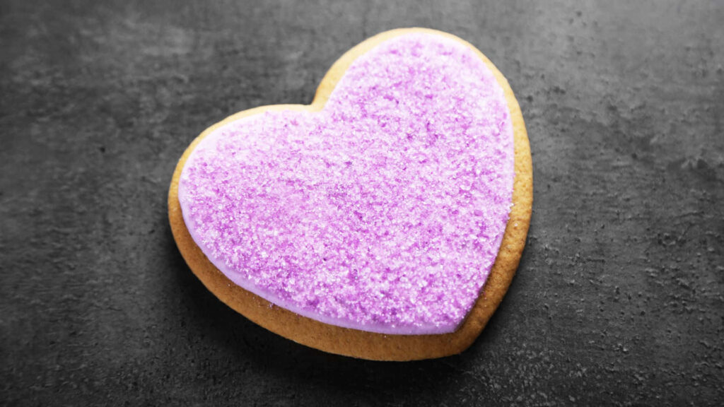 Vibrant Purple Frosted Heart Cookie on Dark Textured Wallpaper