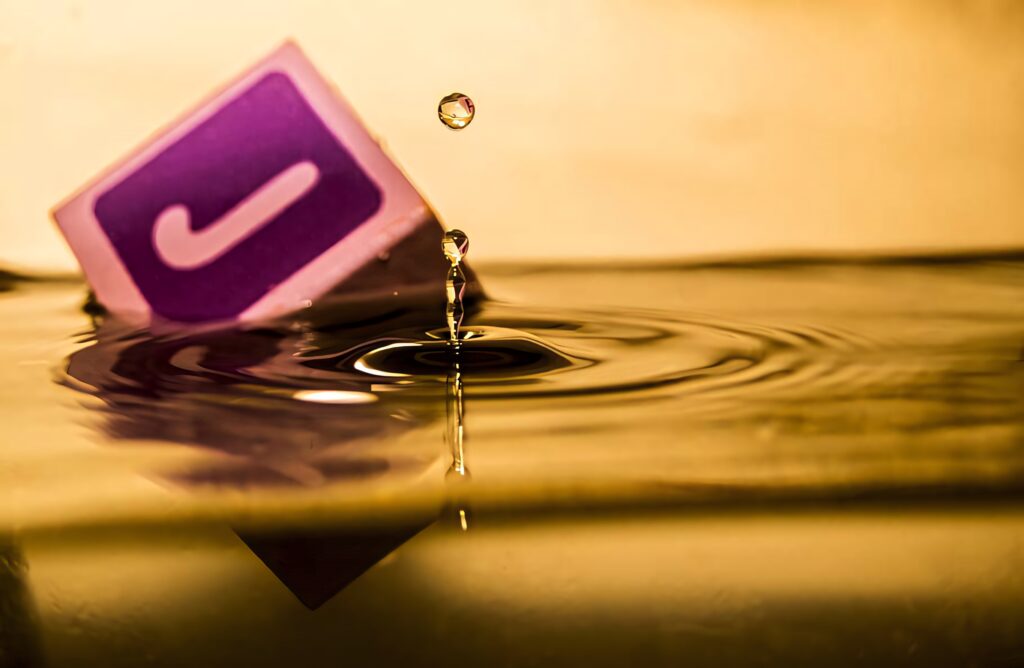 Dynamic Purple Letter J in Liquid with Ripples and Golden Background Wallpaper