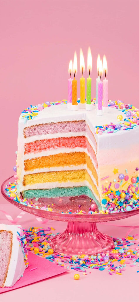 Vibrant rainbow layered cake with colorful candles and sprinkles on soft pink festive background Wallpaper