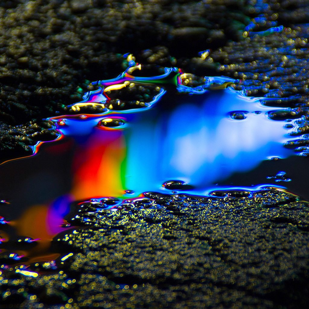 Vibrant rainbow neon light reflection in asphalt puddle artistic urban moody wallpaper background