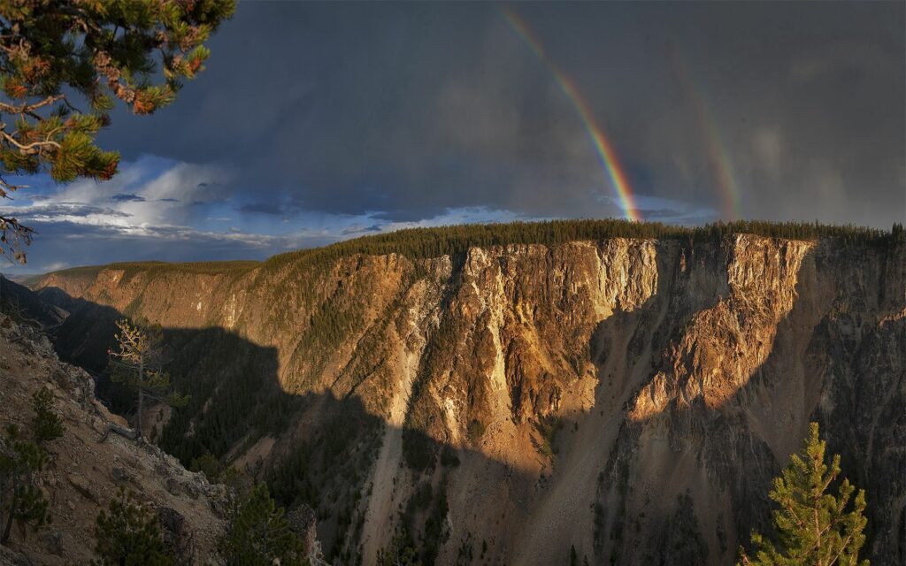 Vibrant rainbow over rugged mountain canyon with dramatic cliffs and dynamic sunlit sky wallpaper