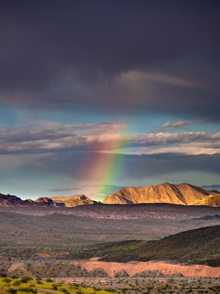 Vibrant rainbow over sunlit mountain peaks and dramatic storm clouds natural landscape wallpaper