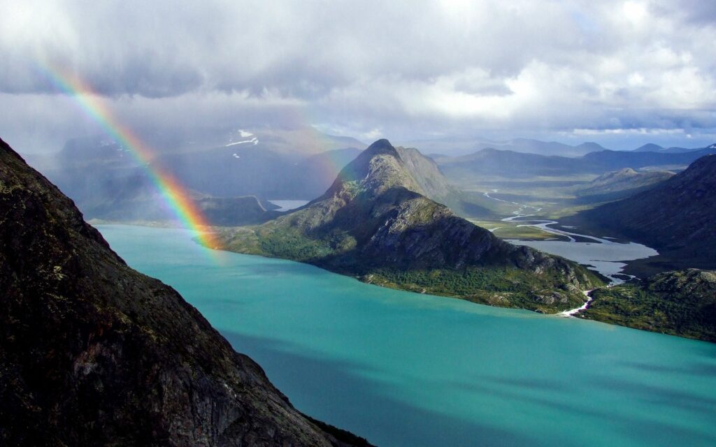 Vibrant rainbow over turquoise ocean rugged mountains lush green landscape with winding rivers Wallpaper
