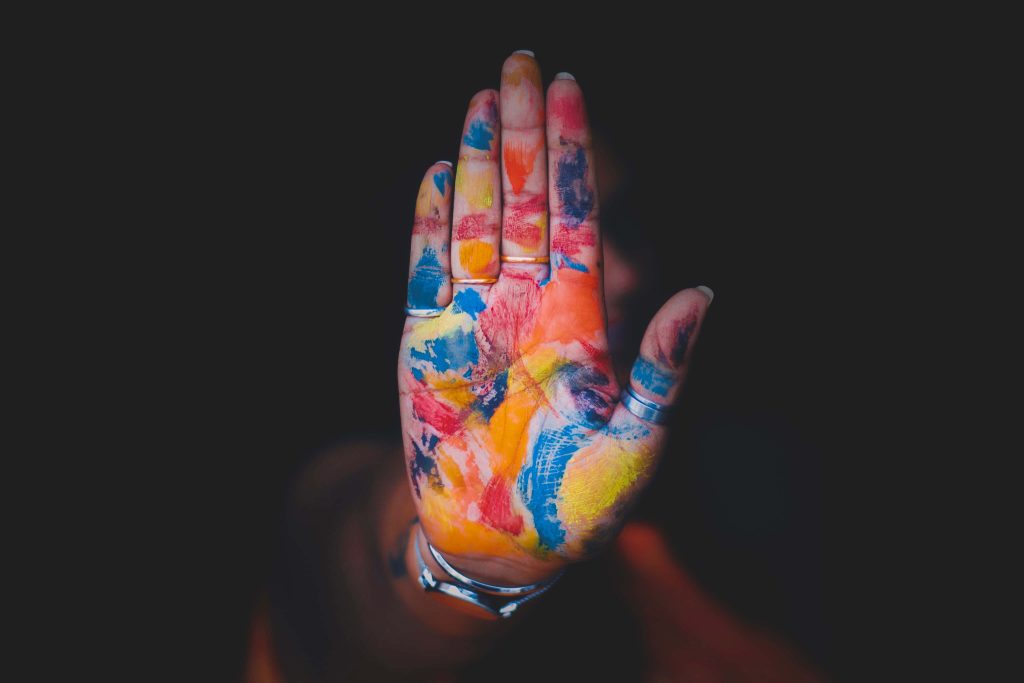 Hand with vibrant rainbow paint and elegant rings making a stop gesture on dark background wallpaper
