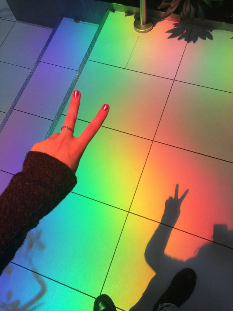Hand making peace sign casting colorful rainbow shadow on tiled floor vibrant wallpaper background