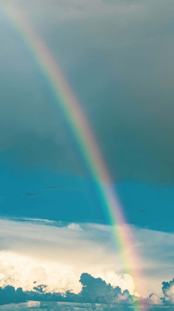 Vibrant rainbow arch over soft clouds sky iPhone wallpaper serene colorful nature background