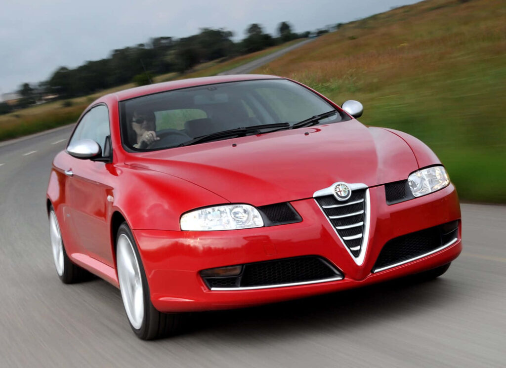 Red Alfa Romeo GT driving on open country road showcasing sleek design and dynamic performance Wallpaper