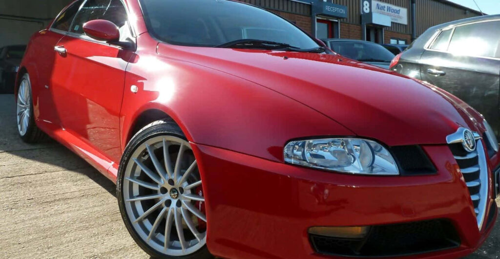 Red Alfa Romeo GT parked in sunlight showcasing sleek design and sporty alloy wheels wallpaper background