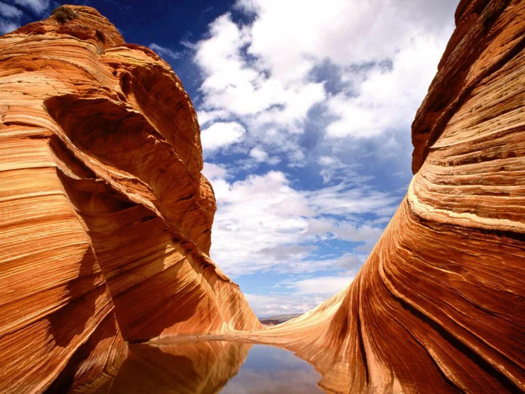 Vibrant red and orange canyon with layered rock patterns reflected in calm water under sky Wallpaper