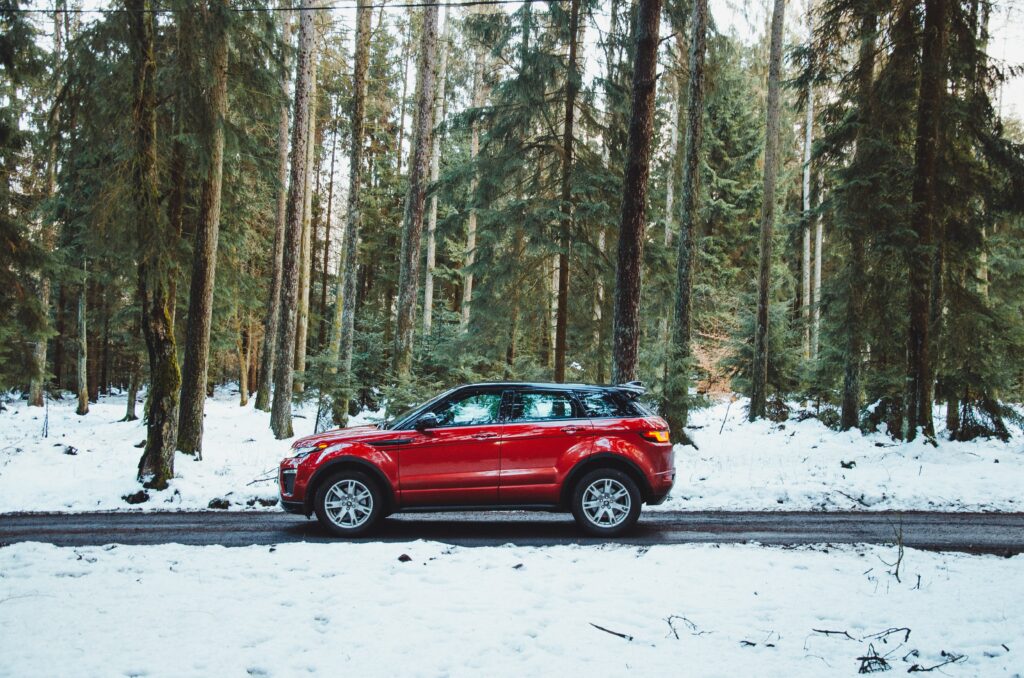 Vibrant Red Car on Road Against Serene Snowy Forest Background Wallpaper