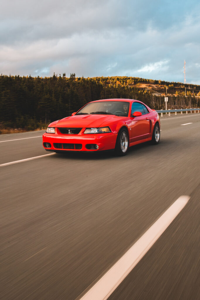 Vibrant Red Car Racing Through Lush Greenery and Blue Sky Adventure Wallpaper