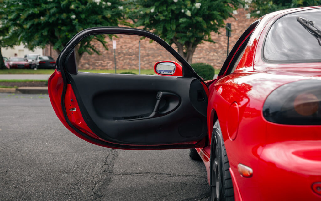 Vibrant Red Car with Open Door: Sleek Interior Amidst Greenery Wallpaper