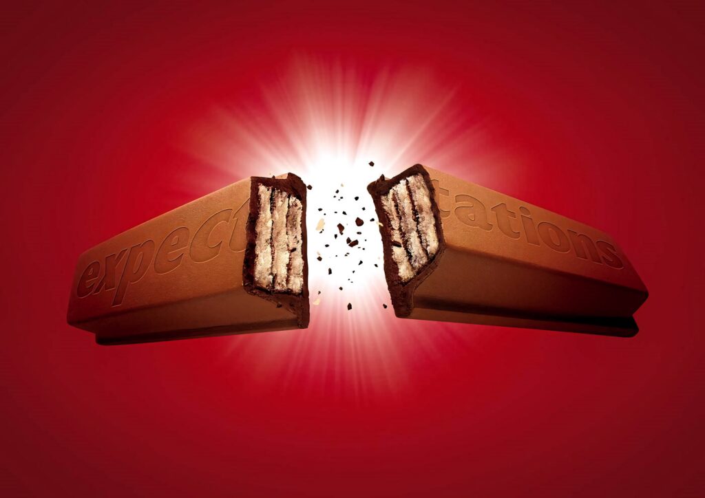 Chocolate bar engraved with expectations splits revealing crispy wafers on vibrant red background wallpaper