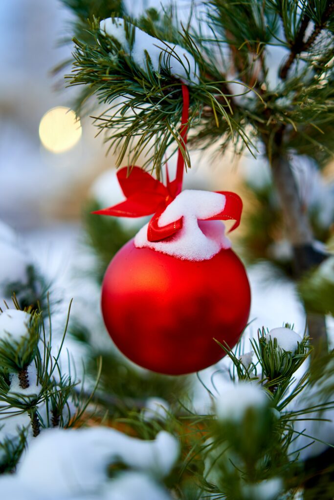 Vibrant Red Christmas Ornament with Snow on Green Tree Branch Background Wallpaper