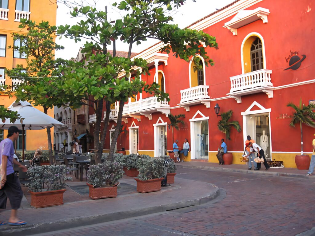 Vibrant red colonial building with white trim in lively Cartagena street scene with greenery Wallpaper