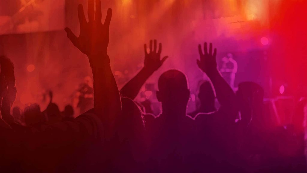 Vibrant concert crowd with raised hands in red lights and smoky atmosphere live music energy wallpaper
