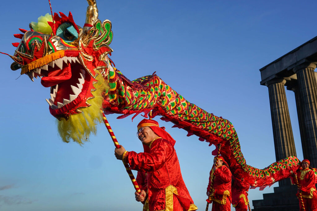Vibrant New Year parade with performers in red and colorful dragon puppet under blue sky wallpaper