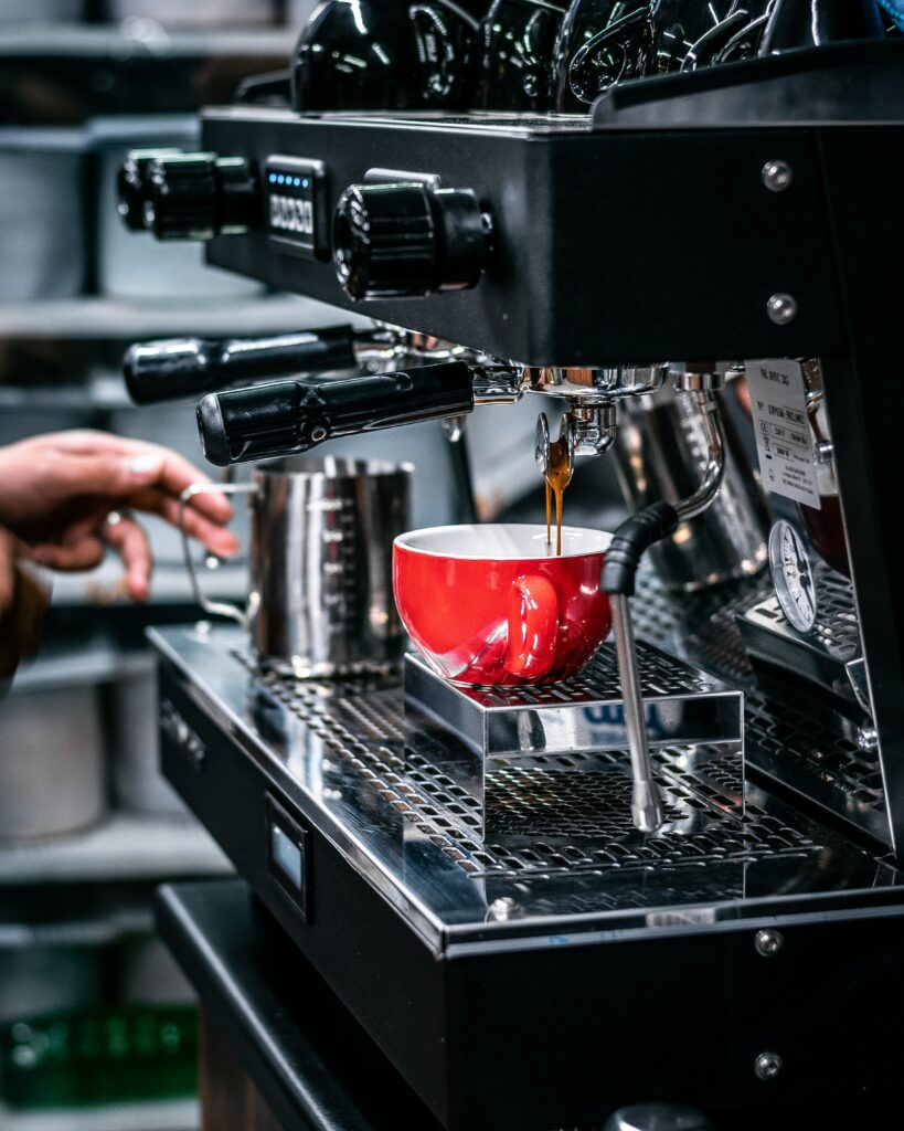 Vibrant Red Coffee Cup Under Machine: Lively Cafe Wallpaper
