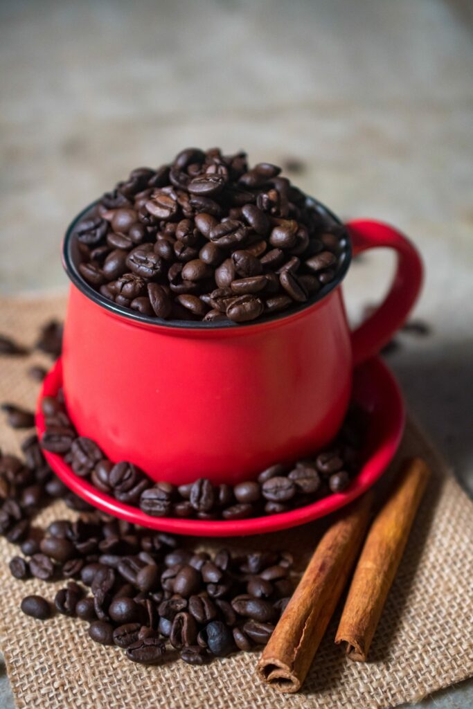 Vibrant Red Cup Filled with Coffee Beans & Cinnamon Sticks Wallpaper