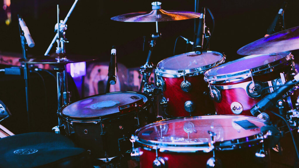 Glossy red drum set with shining cymbals and chrome hardware under dynamic stage lighting Wallpaper