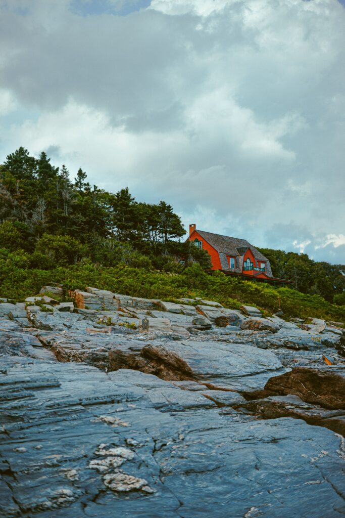Vibrant red house among green trees on stone cliffs under dramatic cloudy sky landscape wallpaper