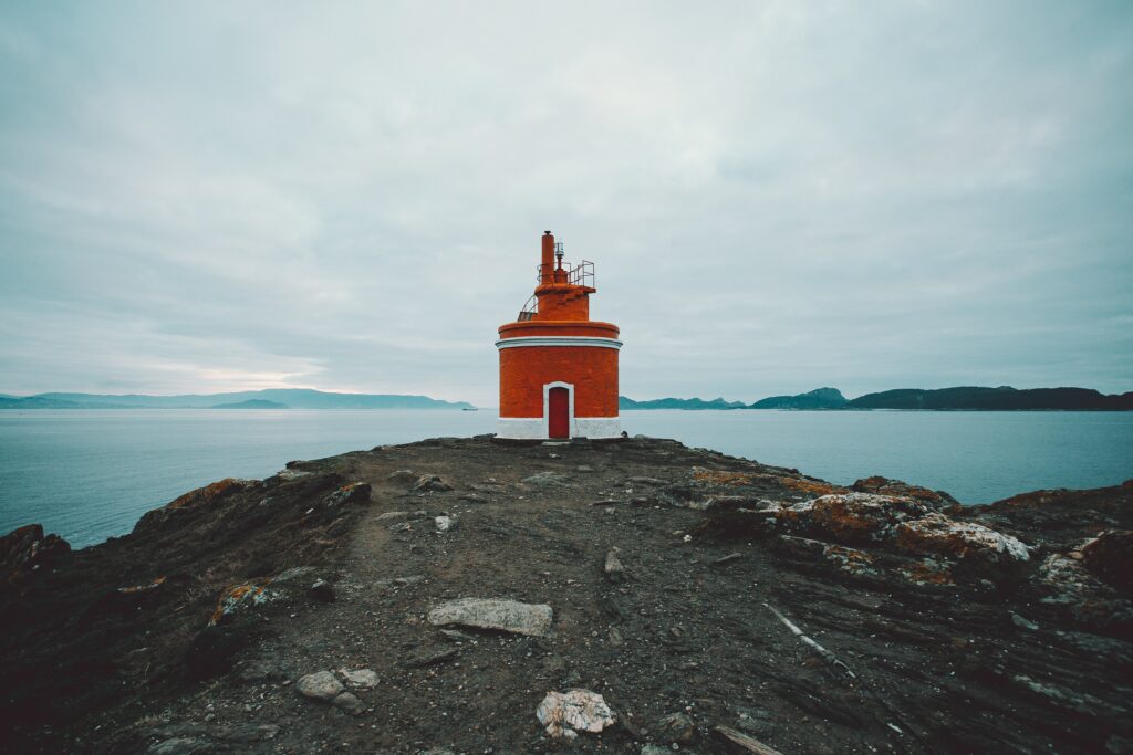 Vibrant red lighthouse on rocky coast with calm blue waters and cloudy sky background wallpaper