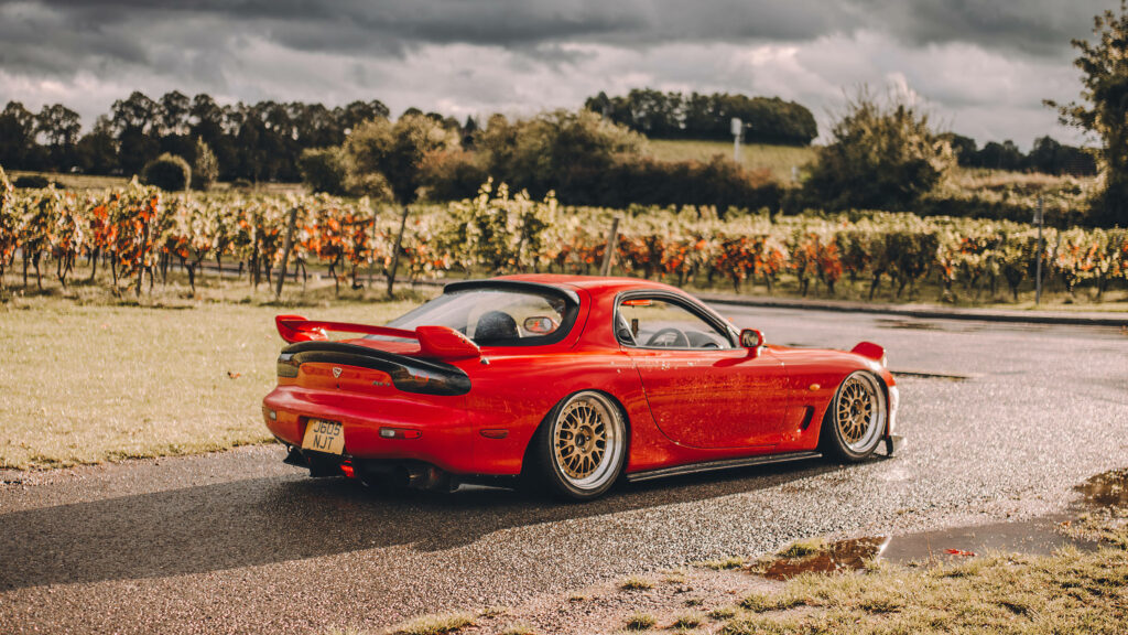 Red Rx-7 Rests Amidst Scenic Garden Landscape - Majestic Vintage Car Image Wallpaper