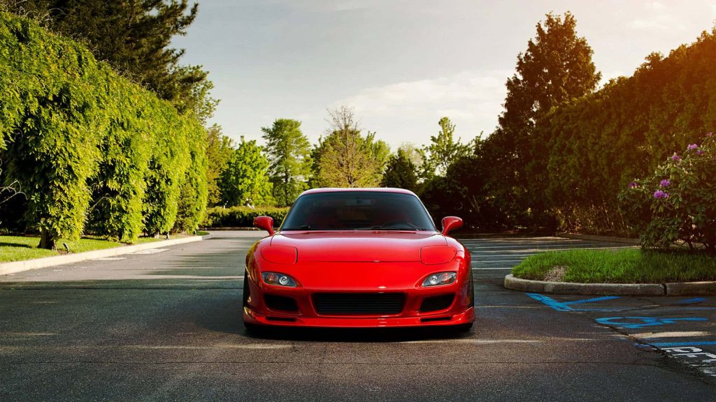 Front view of vibrant red Mazda RX-7 FD in golden hour light with lush trees background outdoors Wallpaper