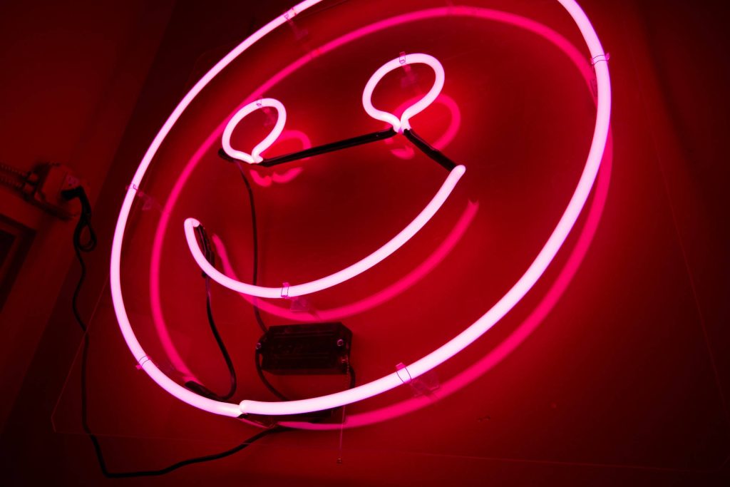 Vibrant red neon smiley face wallpaper with glowing light and industrial wiring background