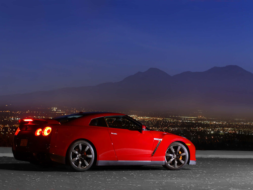 Red Nissan R35 GTR 2009 parked at twilight cityscape with mountains dynamic powerful car wallpaper