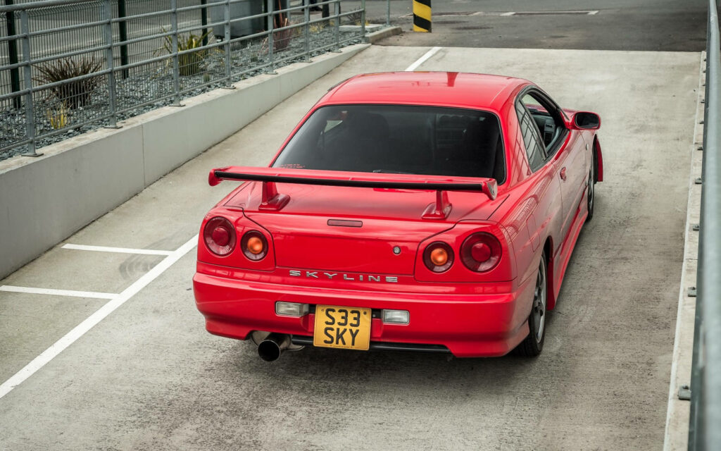 Vibrant Red Nissan Skyline GTR R34 Wallpaper in Modern Setting