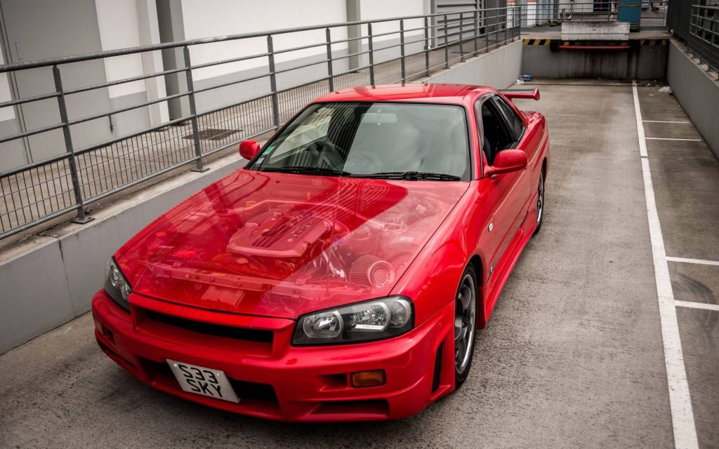 Front-angle view of vibrant red Nissan Skyline GT-R R34 with clear hood showing engine details Wallpaper