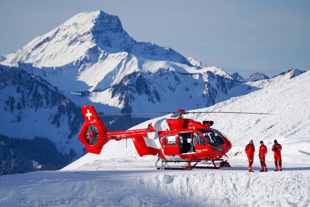 Red Rega rescue helicopter on snowy Swiss mountain with crew in vibrant red uniforms Wallpaper