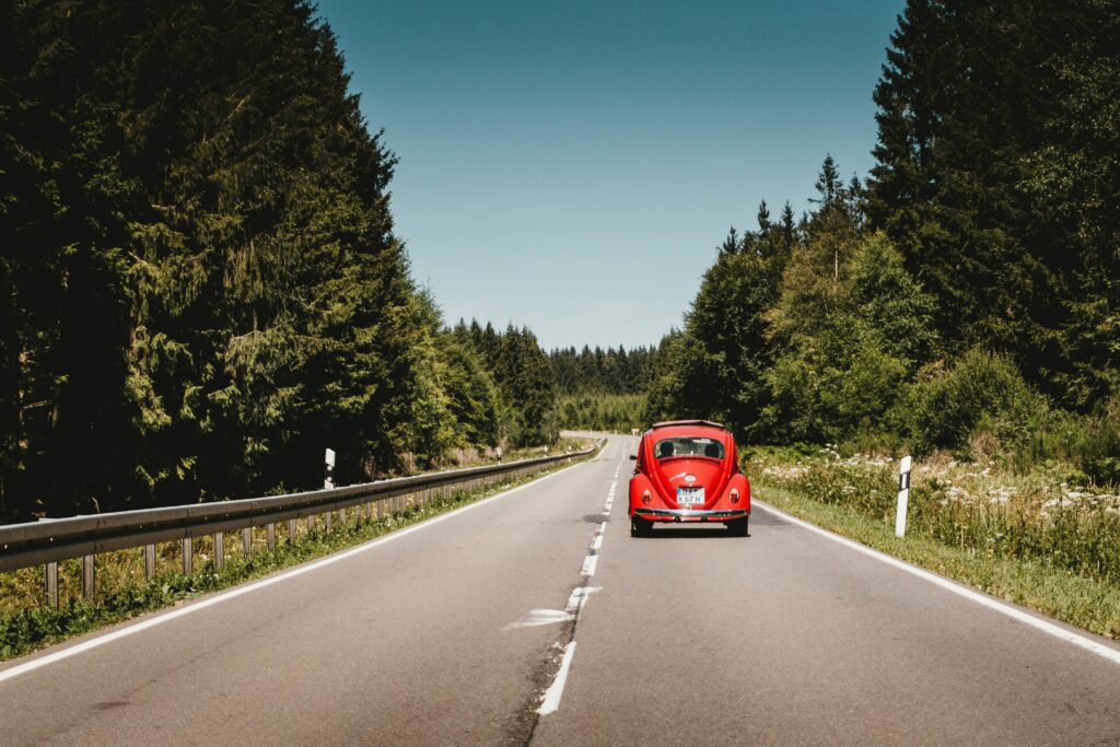 Red Retro Car on Scenic Road: Adventure Amidst Greenery & Skies Wallpaper