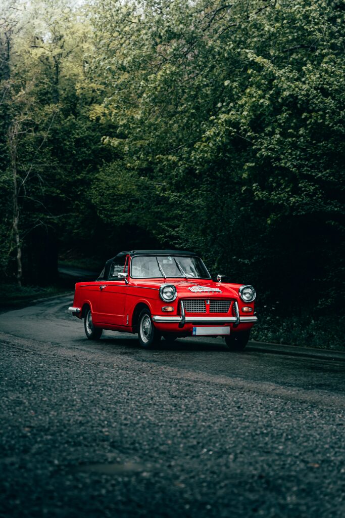 Vibrant Red Retro Car on Winding Road in Lush Greenery Wallpaper