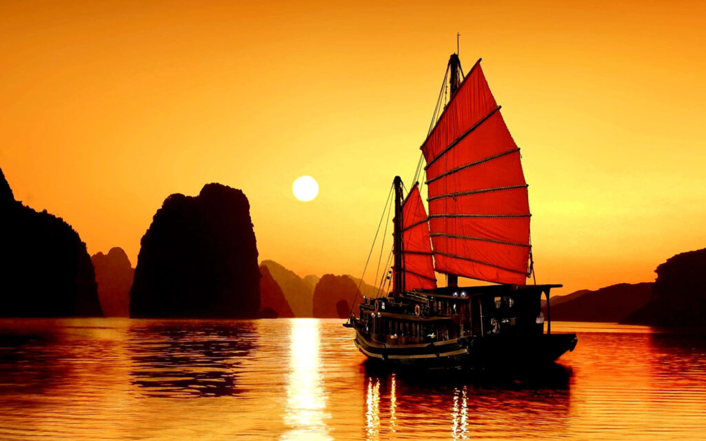 Vibrant red ship sails Halong Bay at sunset with limestone cliffs Vietnam scenic wallpaper background