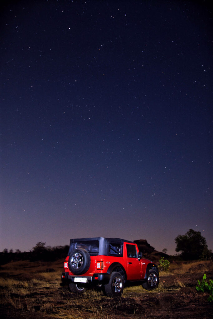 Vibrant red Thar on rugged terrain under starry night sky ultra high 4K adventure wallpaper
