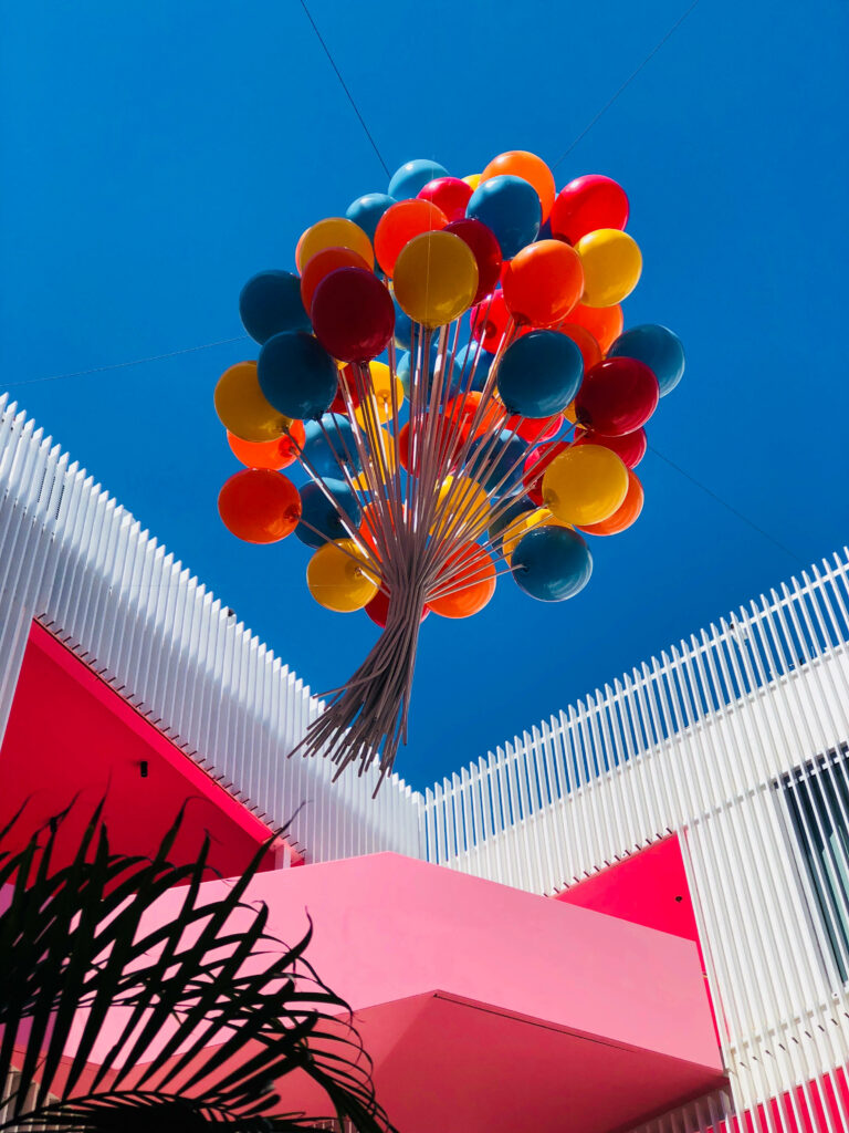Colorful red yellow and blue balloons floating over modern building courtyard blue sky background Wallpaper