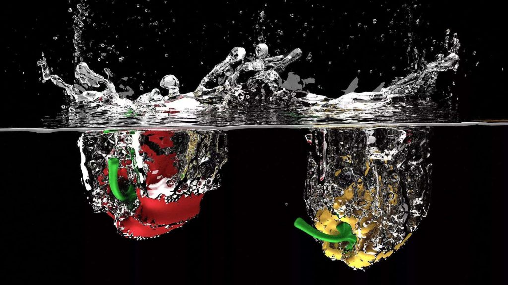 Red and yellow bell peppers splashing into water with bubbles and spray on black background Wallpaper