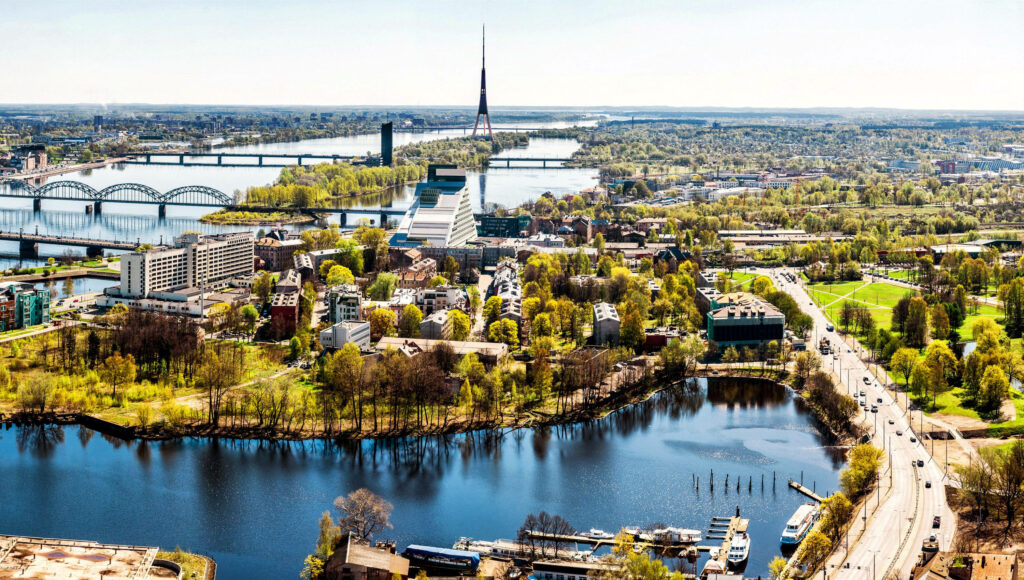 Panoramic Riga cityscape wallpaper featuring historic architecture lush greenery and river bridges