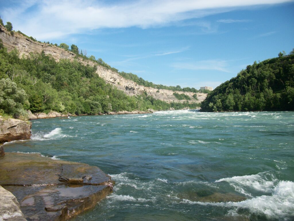 Vibrant river winding through lush green forest with rocky cliffs and clear blue skies wallpaper
