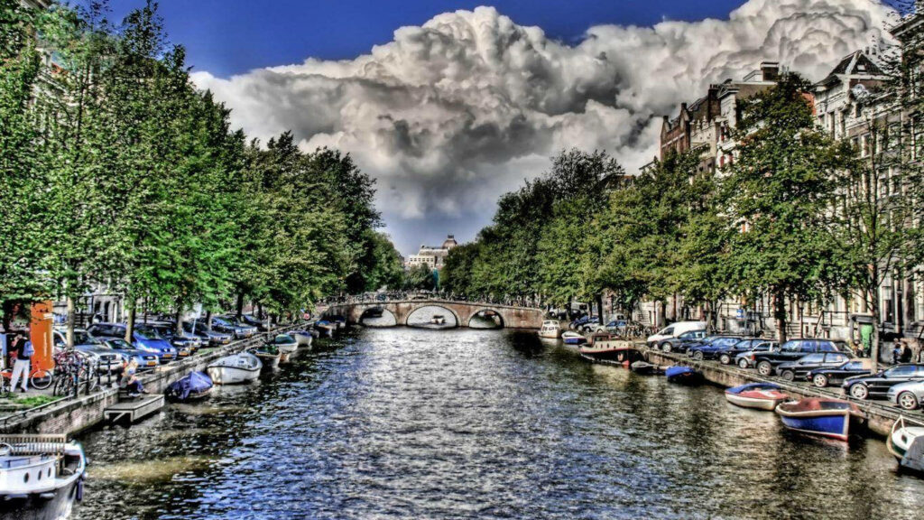 Vibrant Riverside Cityscape Wallpaper: Lush Greenery & Cloudy Sky