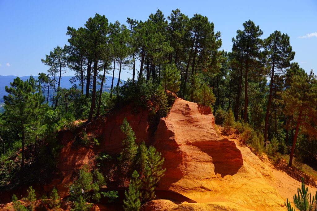 Vibrant ochre rock formations of Roussillon with green trees and clear blue sky wallpaper background