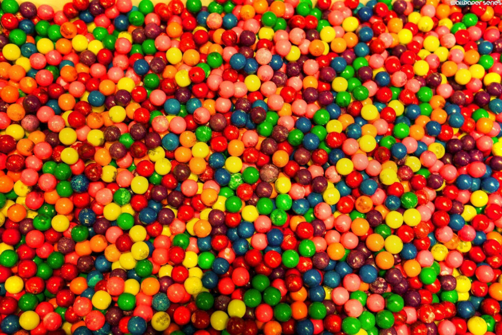 Colorful Skittles candy scattered background with glossy red green yellow orange purple hues wallpaper