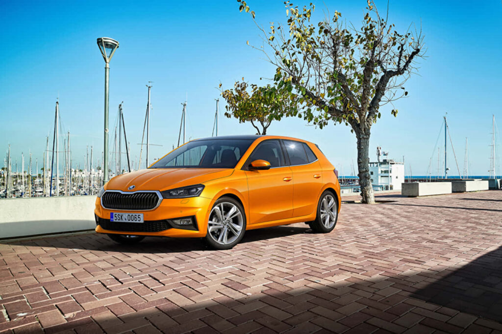 Vibrant Skoda Fabia Wallpaper: Orange Hatchback by Serene Waterfront