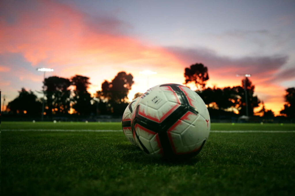 Vibrant Sunset Soccer Field Wallpaper with Grass & Soccer Balls